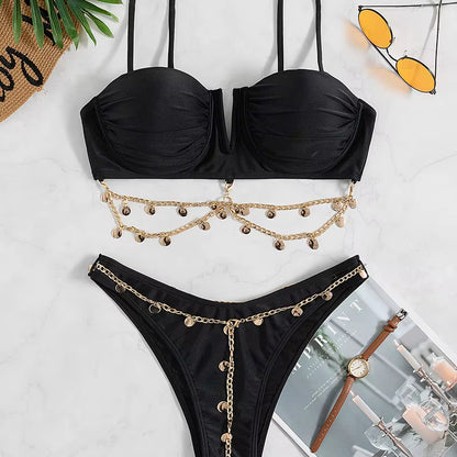Black bikini set with gold chain details on a styled white surface.