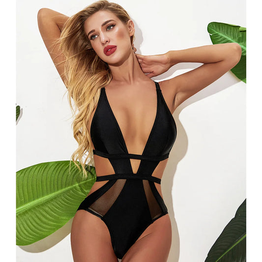 A woman wearing a black one piece trikini swimsuit with tie details and a deep V-neckline.